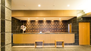 A reception area with a wooden counter, two wooden benches, a decorative flower arrangement, and a check-in station. - Dormy Inn Premium Wakayama Natural Hot Spring (Wakayama)