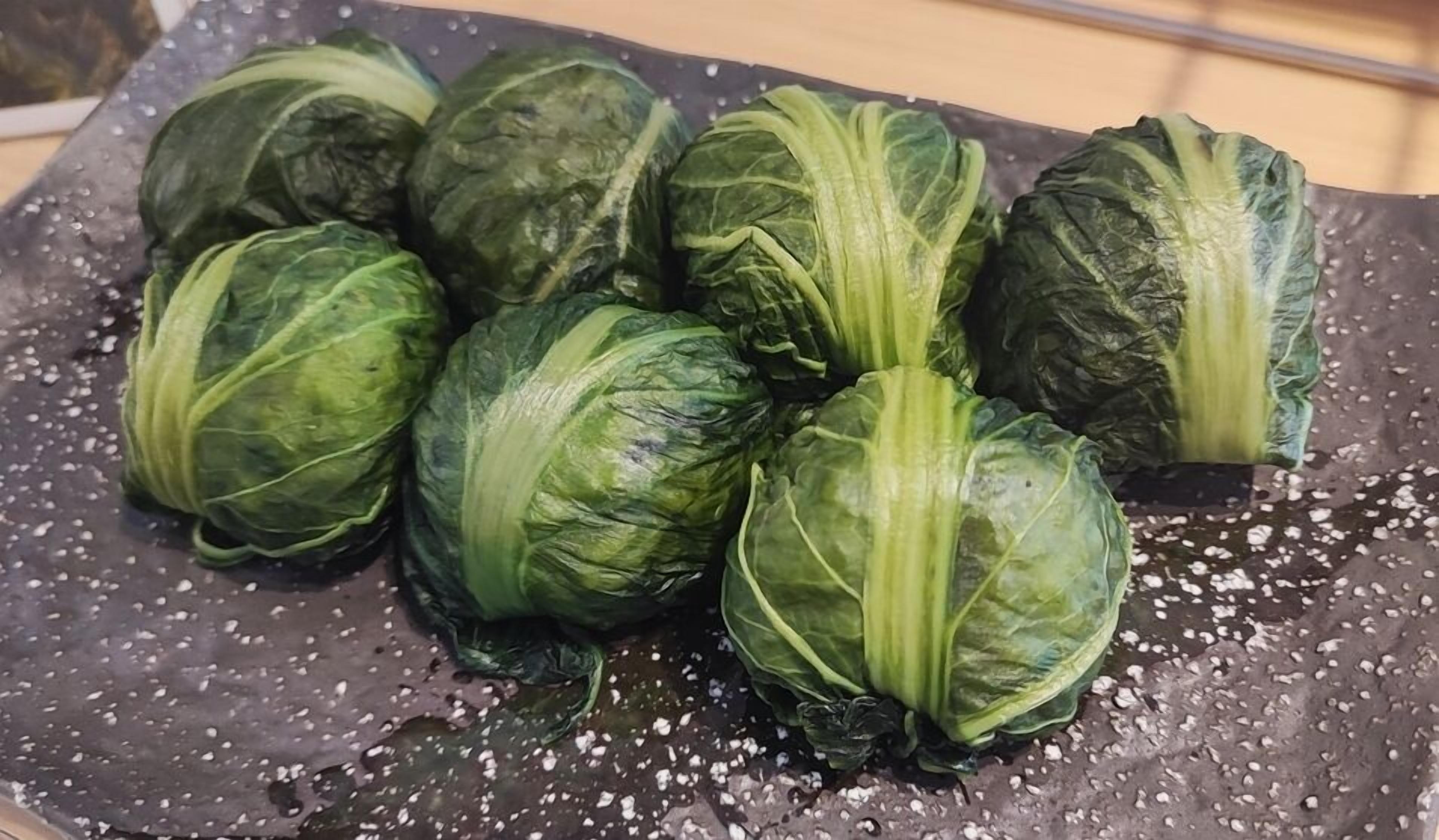 Uma travessa com repolhos recheados cozidos em um prato escuro com gotas d'água.
