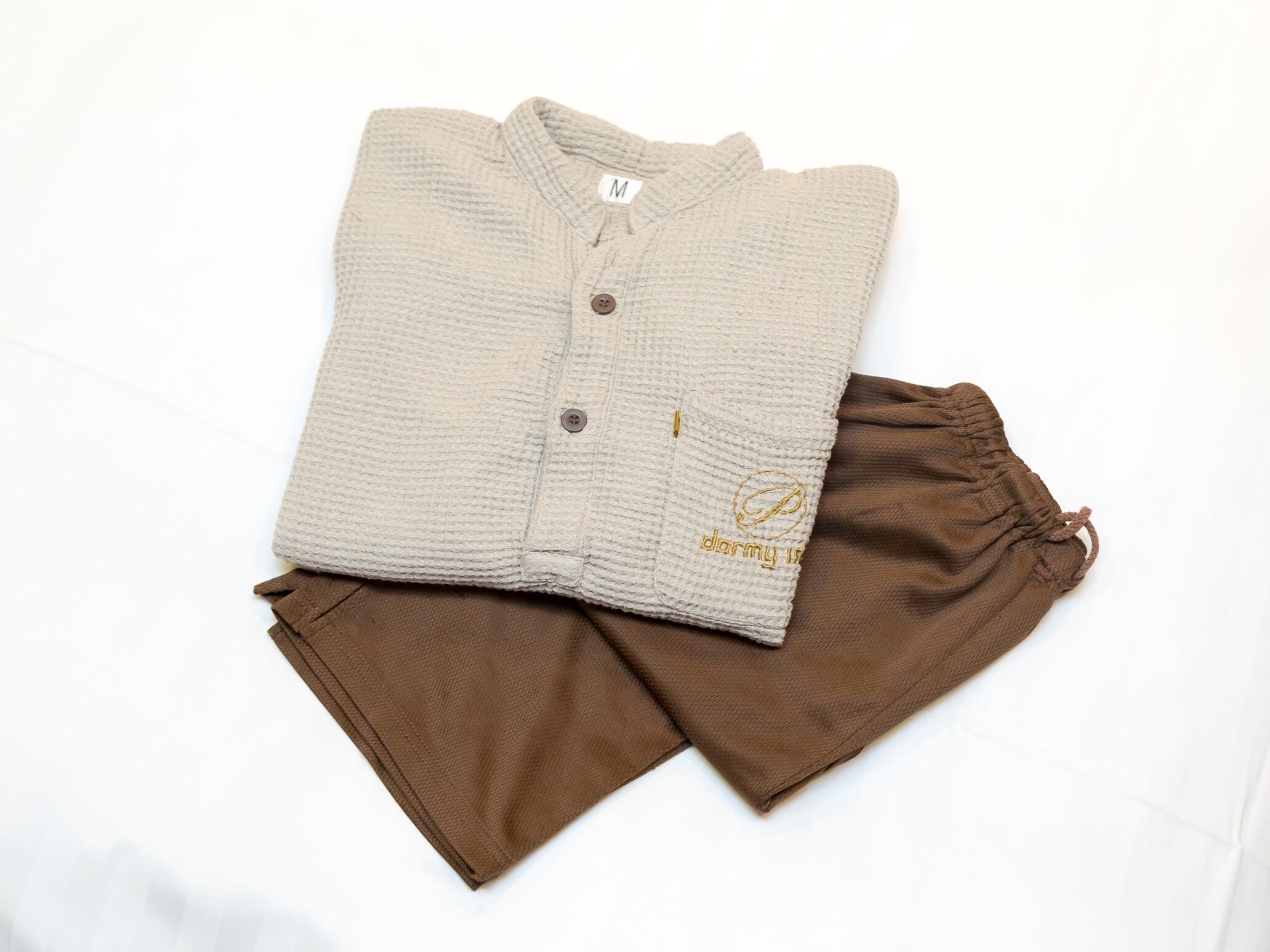 Un cárdigan beige bien doblado y pantalones marrones sobre una superficie blanca.