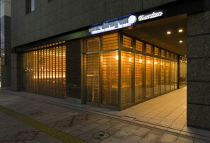 A hotel entrance with a glass facade, a visible reception desk, and a sign above the entrance.