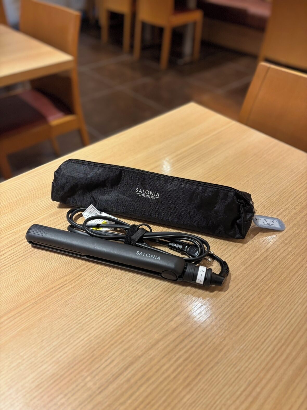 A black electronic device with a cable and a black carrying case on a wooden table.