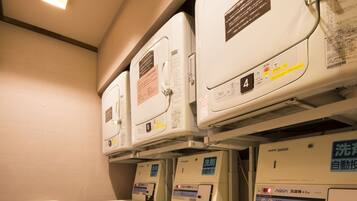 A laundry room with multiple washing machines and dryers, a metal shelf unit, and a wooden floor.