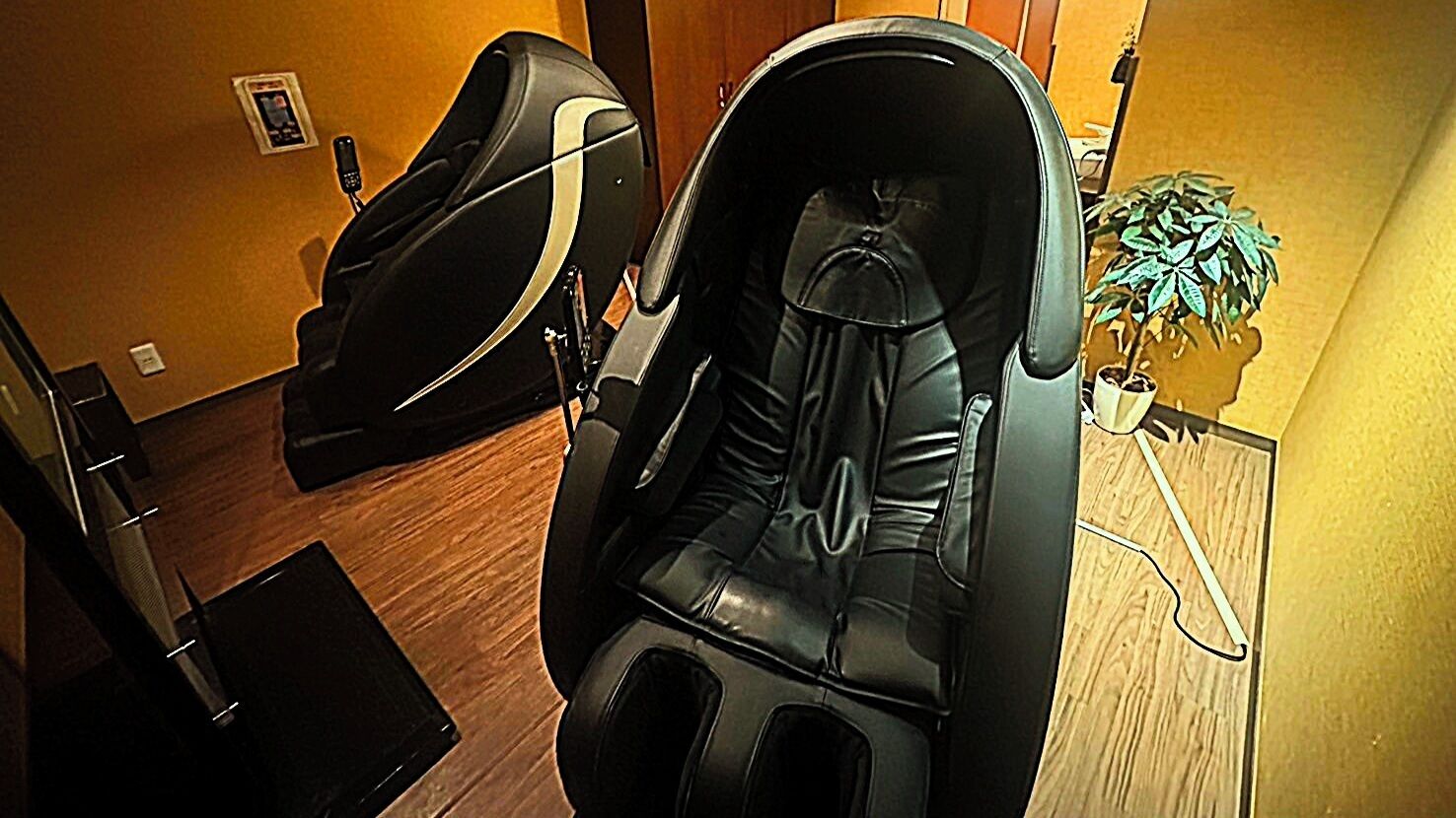 A massage chair in a room with wooden flooring and a potted plant.