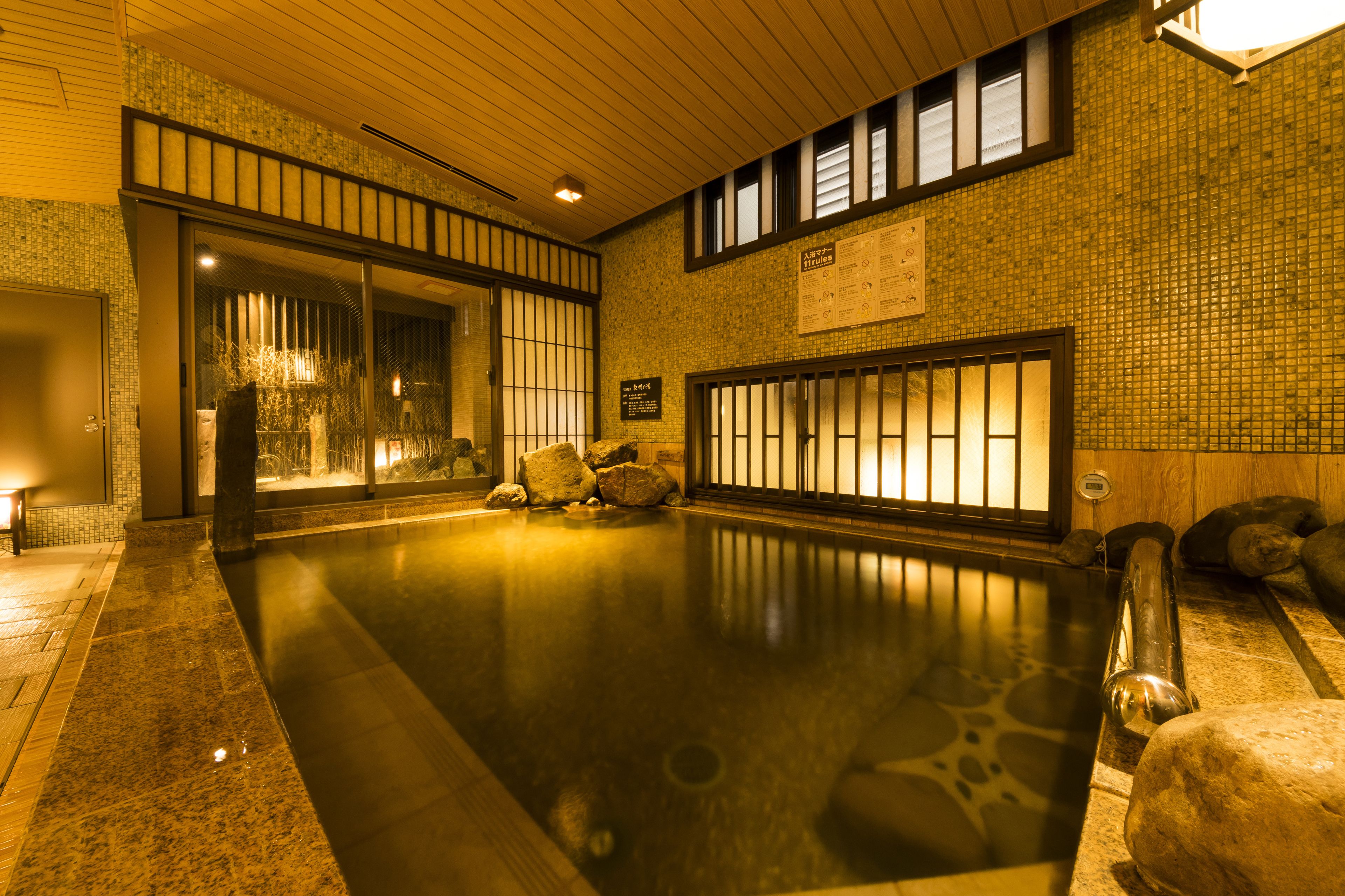A traditional Japanese onsen with a wooden interior, a stone bath, and a tiled wall with a sign.