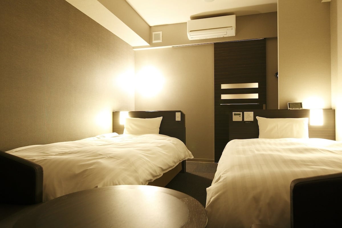 A hotel room with two beds, a round table, and an air conditioning unit.