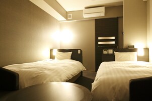 Quarto de hotel com duas camas, uma mesa redonda e um aparelho de ar condicionado.