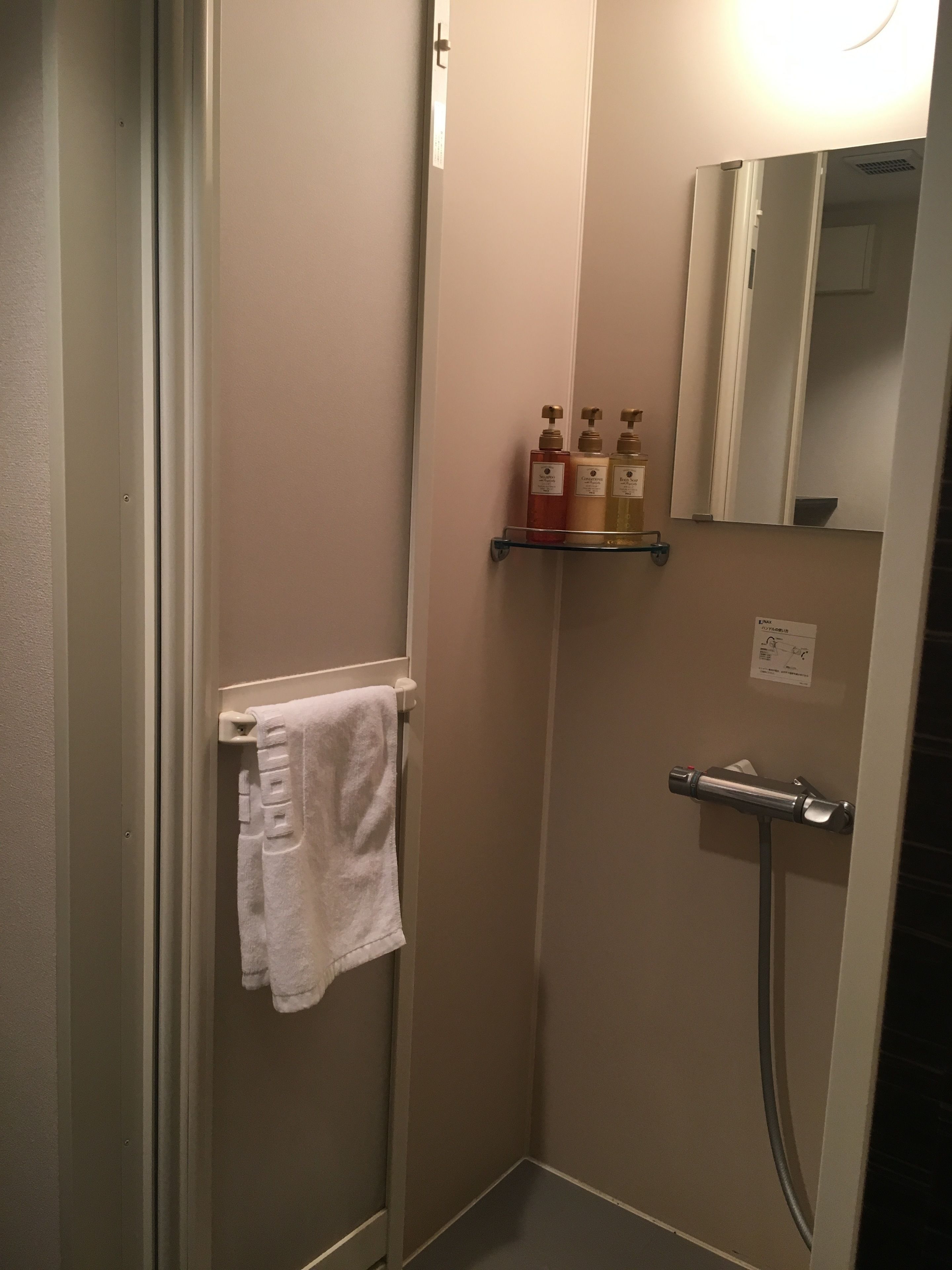 A small bathroom with a glass shower enclosure, a towel rack with a white towel, and a shelf with toiletries.
