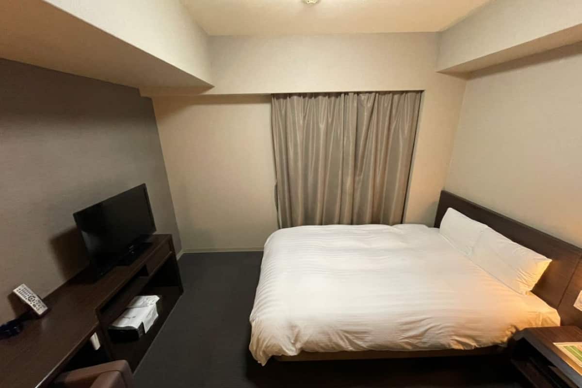A hotel room with a bed, a TV, a desk, and a curtain.