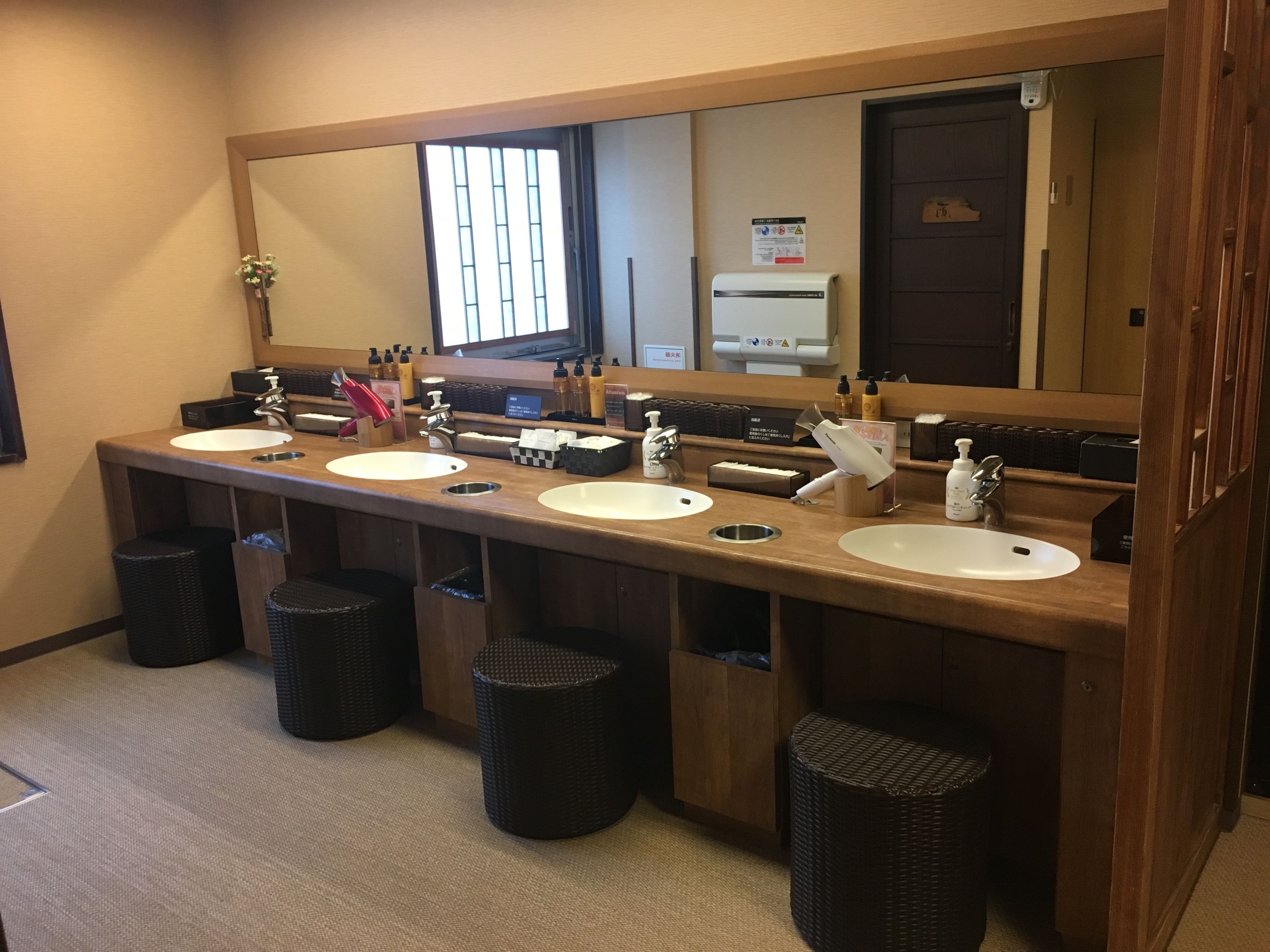 A hotel bathroom with three sinks, a large mirror, and black waste baskets.
