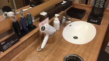 A bathroom with a wooden vanity, a white sink, a Panasonic hair dryer, and various toiletries.