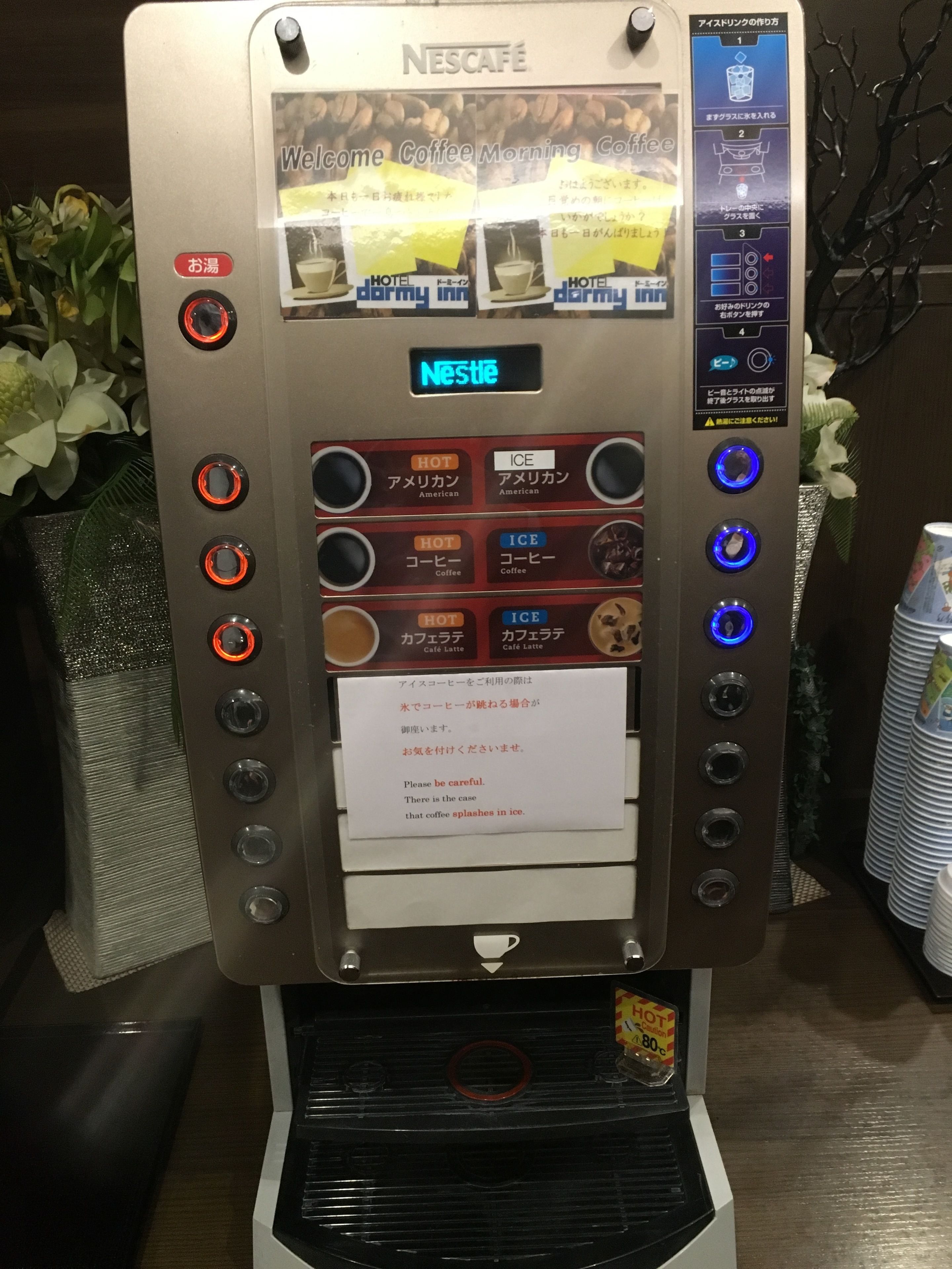 Une machine à café Nescafé offrant de nombreuses options de boissons, notamment du café chaud et du café glacé, ainsi qu’un avertissement concernant les éclaboussures de café dans la glace.