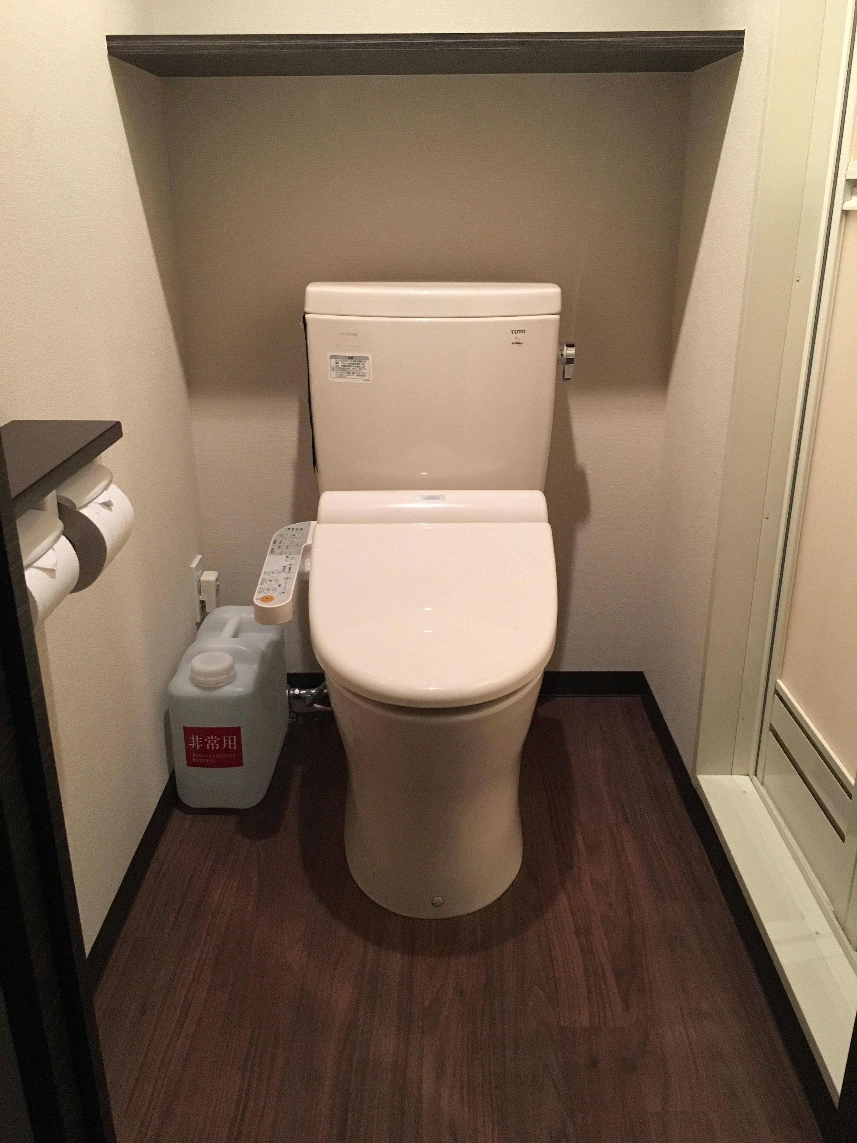 A compact bathroom with a white toilet, a paper towel dispenser, and a large container of toilet paper.