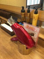 Zona de recepción de un hotel, con un mostrador de madera que exhibe diversos artículos de aseo y un secador de pelo rojo.