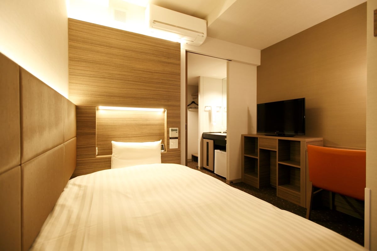 A hotel room with a bed, a TV, a desk, and a chair.