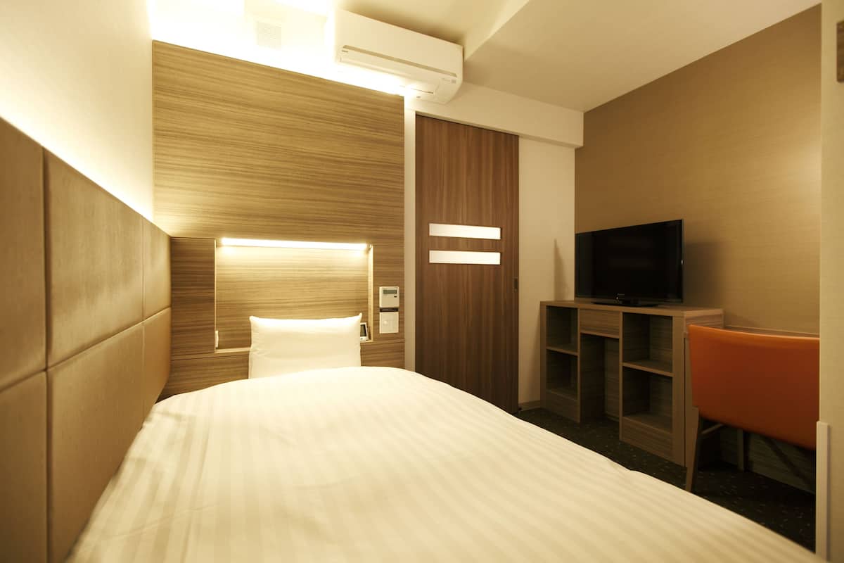A hotel room with a large bed, a TV, a desk, and a chair.