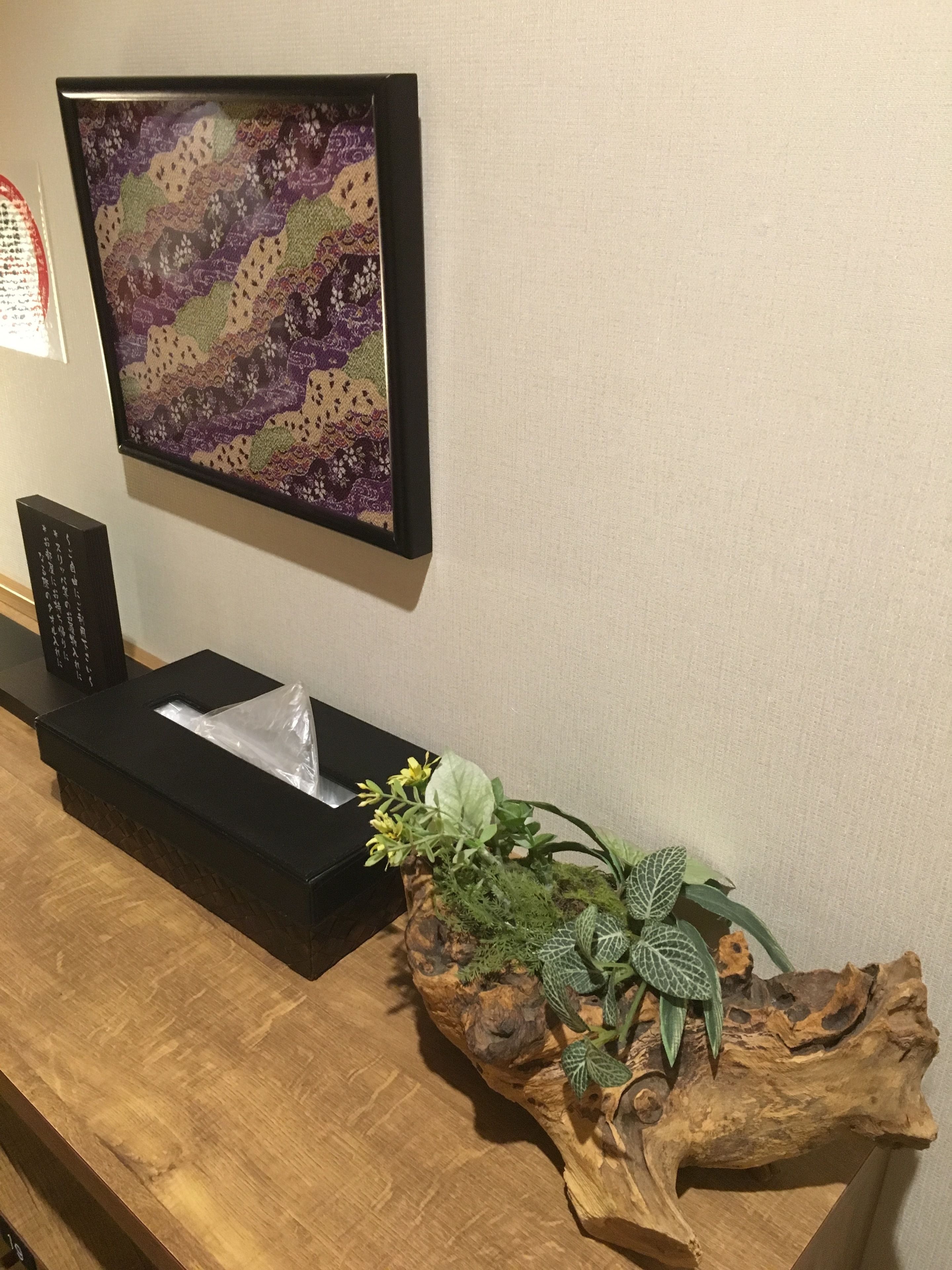 A wooden reception desk with a framed artwork, a black speaker, and a potted plant.