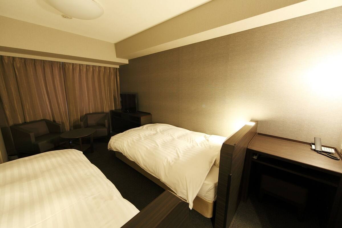 A hotel room with two beds, a desk, a chair, a television, and a curtain.