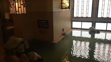 A traditional Japanese onsen with a tiled wall, a wooden bench, and a stone basin.