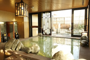 Un onsen japonais traditionnel, avec un intérieur en bois, une source d’eau chaude entourée de pierres et une vue sur le jardin extérieur.