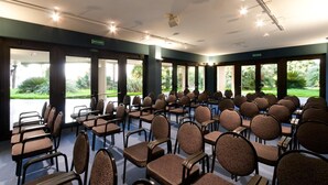 A conference room with rows of chairs and tables, large windows with a view of greenery, and ceiling lights. - Hotel San Michele (Caltanissetta)
