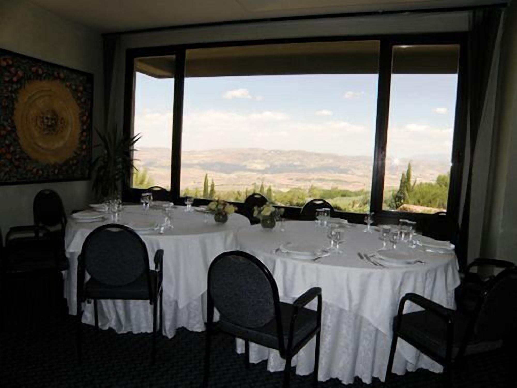 A dining area with round tables set for four, large windows offering a view of a mountainous landscape.