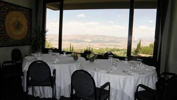 A dining area with round tables set for four, large windows offering a view of a mountainous landscape.