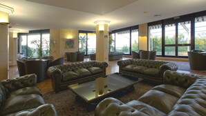 A spacious lobby with leather sofas, a glass coffee table, and large windows offering a view of the outdoors. - Hotel San Michele (Caltanissetta)