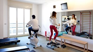A fitness room with exercise equipment, a large mirror, and a television. - Hotel San Michele (Caltanissetta)