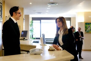 A reception desk with a phone, a digital screen, and a small table with a bell. - Hotel San Michele (Caltanissetta)