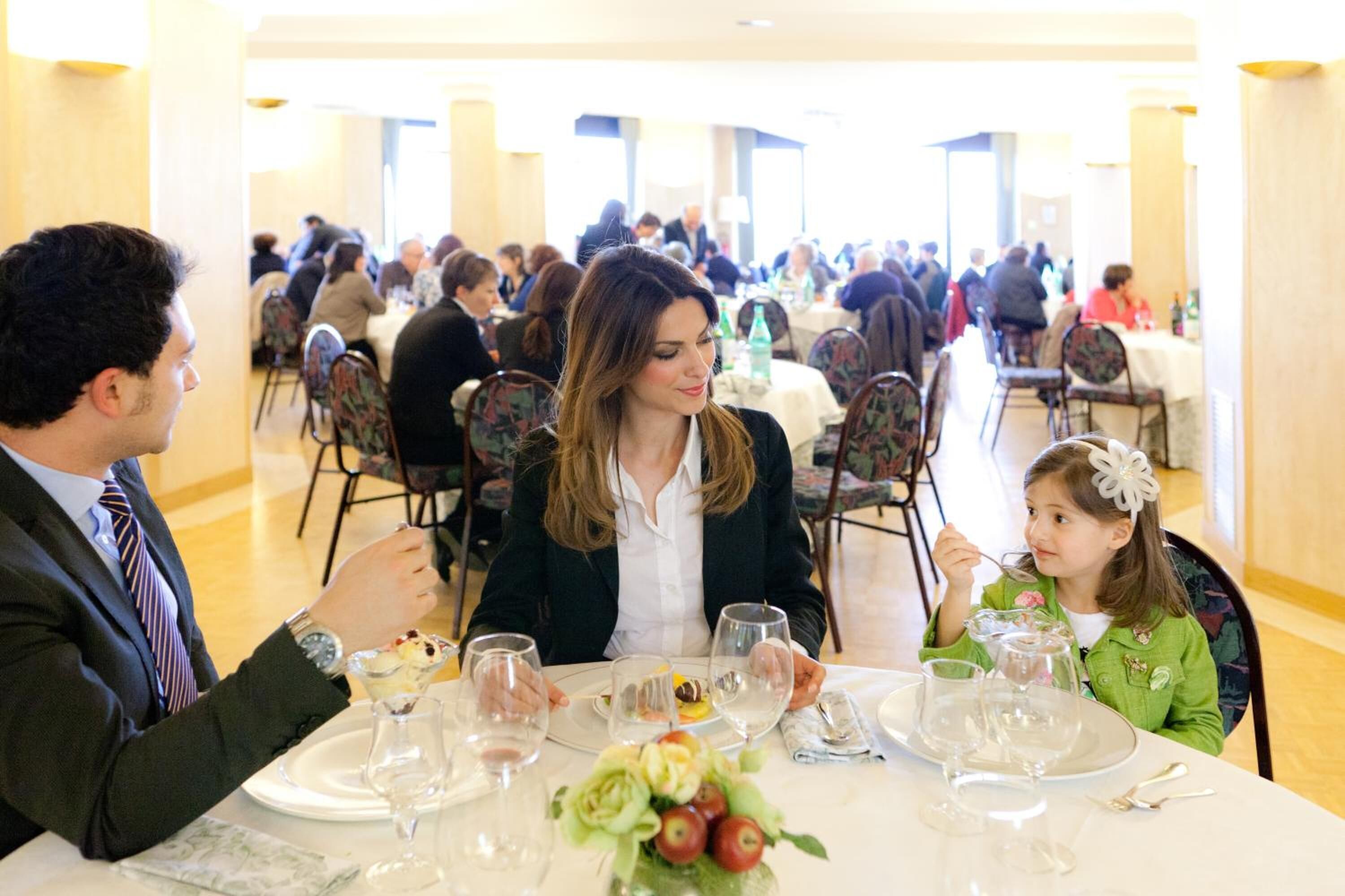 Una sala da pranzo formale con diversi tavoli, sedie e ospiti.