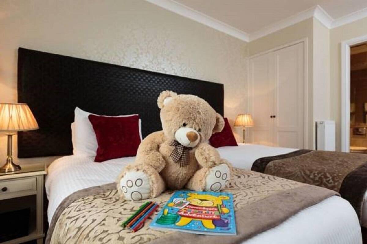A hotel room with a large bed, a teddy bear, and a children's book on the bed.