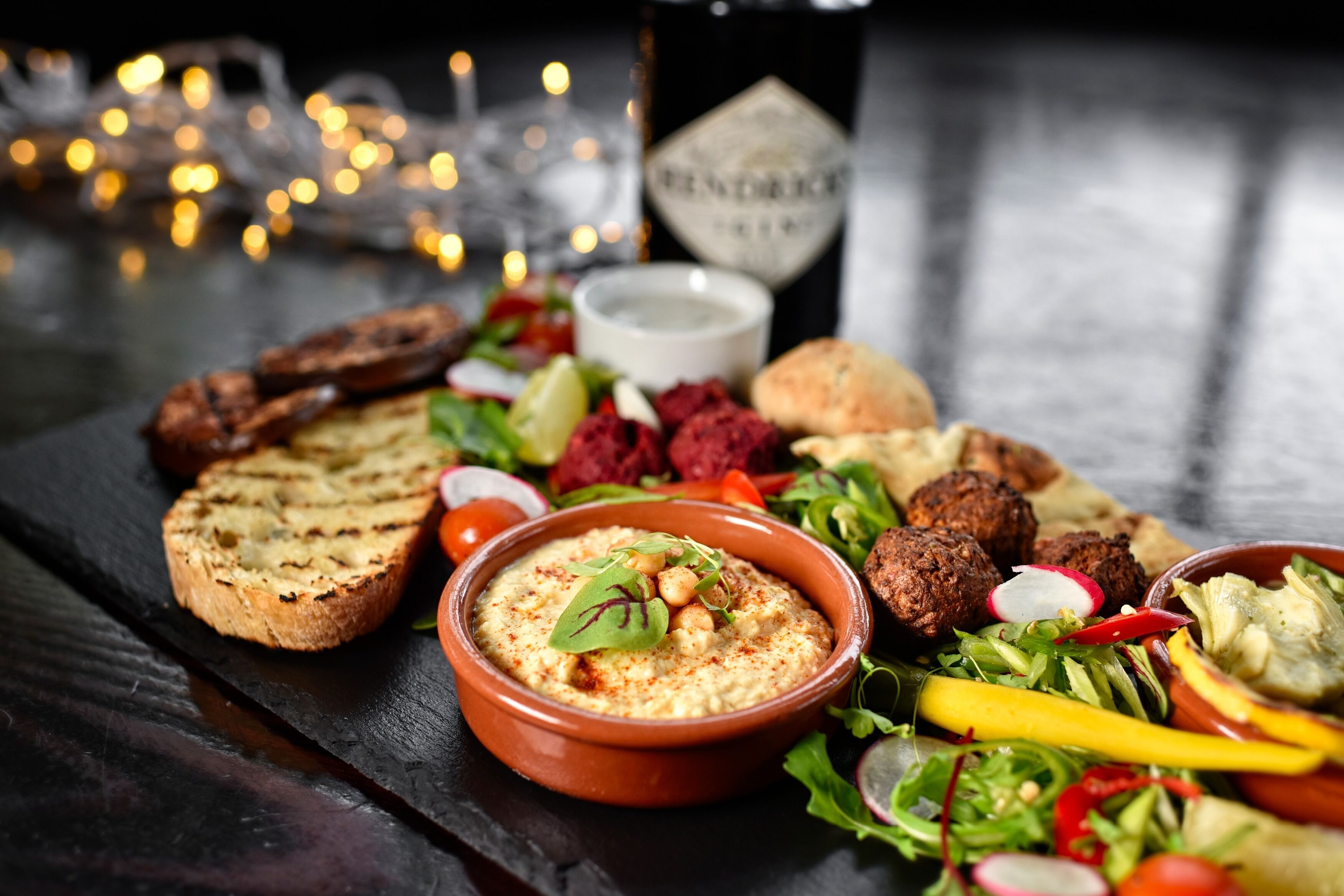 Una mesa con diversos alimentos, como pan, hummus, ensalada y albóndigas.