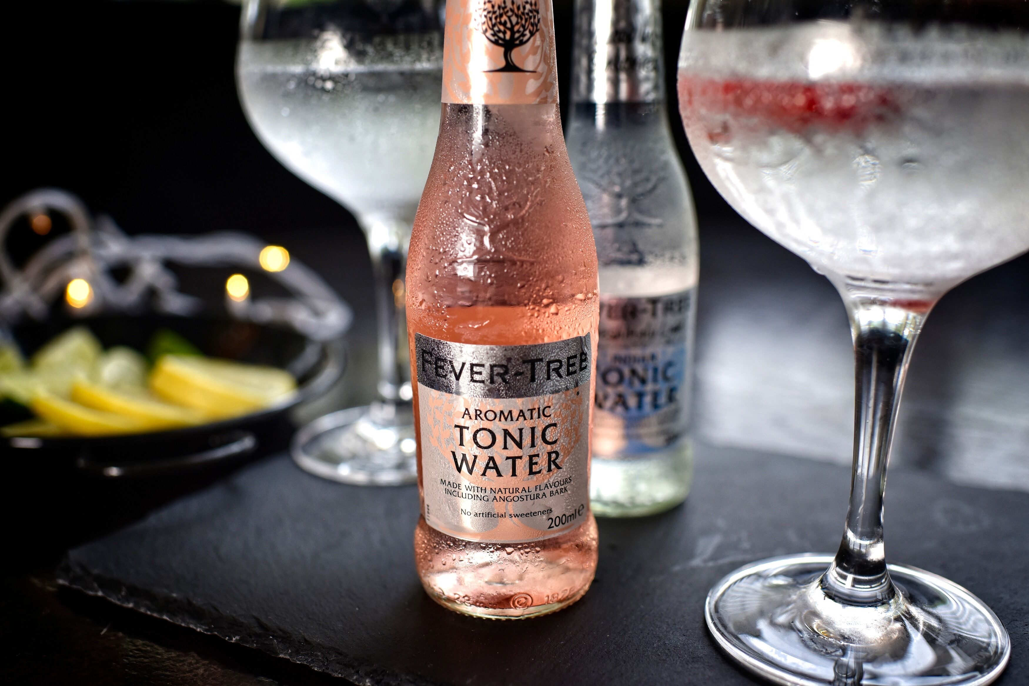 Een fles Fever-Tree Aromatische Tonic Water en een glas water op een zwarte ondergrond.