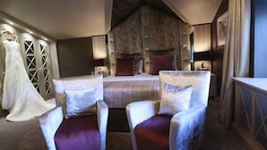 Un dormitorio con una cama grande, dos sillones, un aparador y un armario donde se ve un vestido.