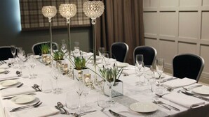 Mesa de comedor dispuesta para un evento formal, con candelabros de cristal, manteles blancos y cubertería de plata.