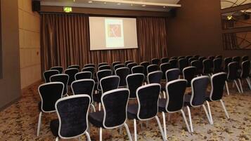 A conference room with rows of black chairs, a projection screen, and a carpeted floor.
