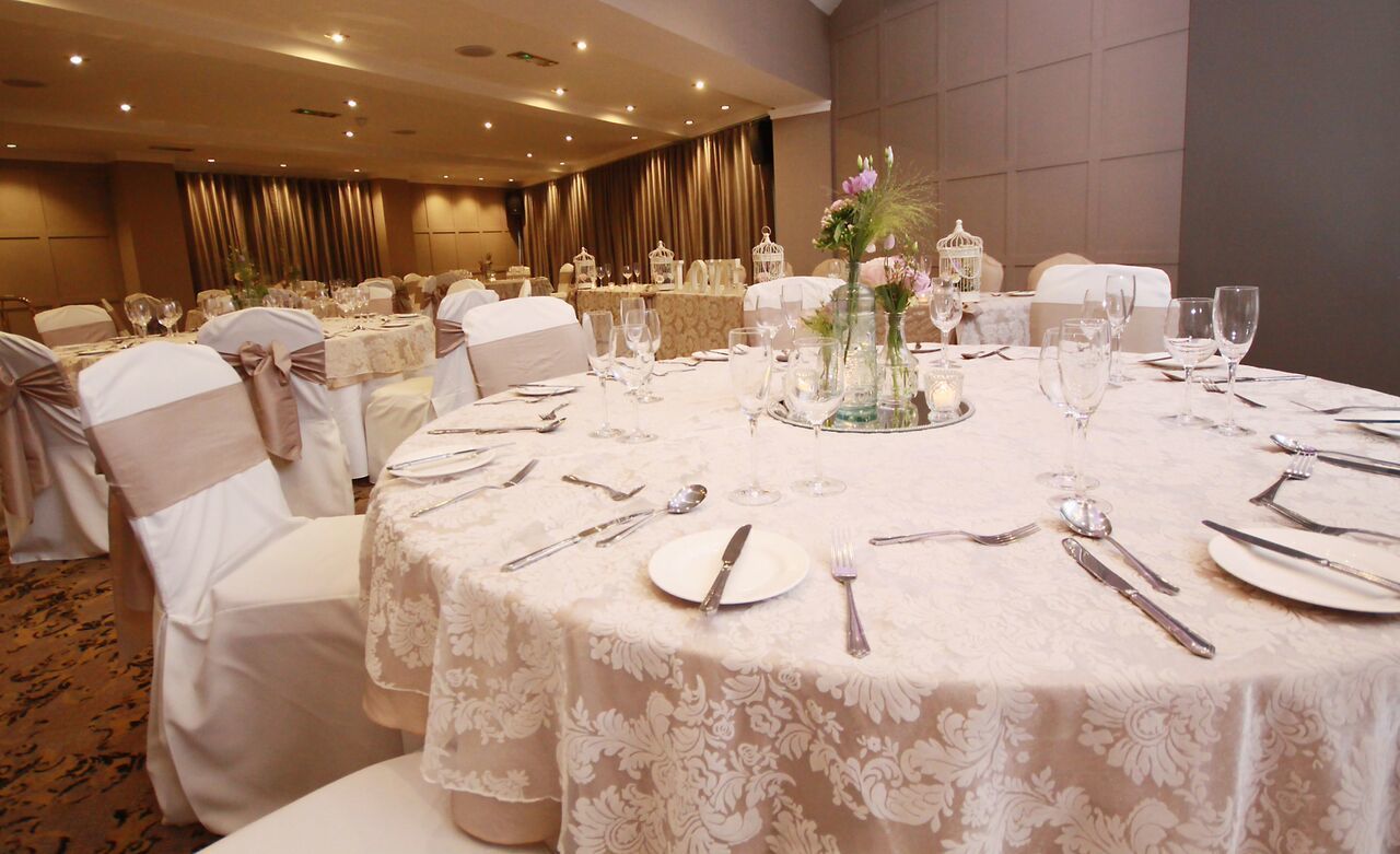 Un salón de banquetes con mesas redondas dispuestas para un evento formal, con manteles blancos y centros de mesa florales.