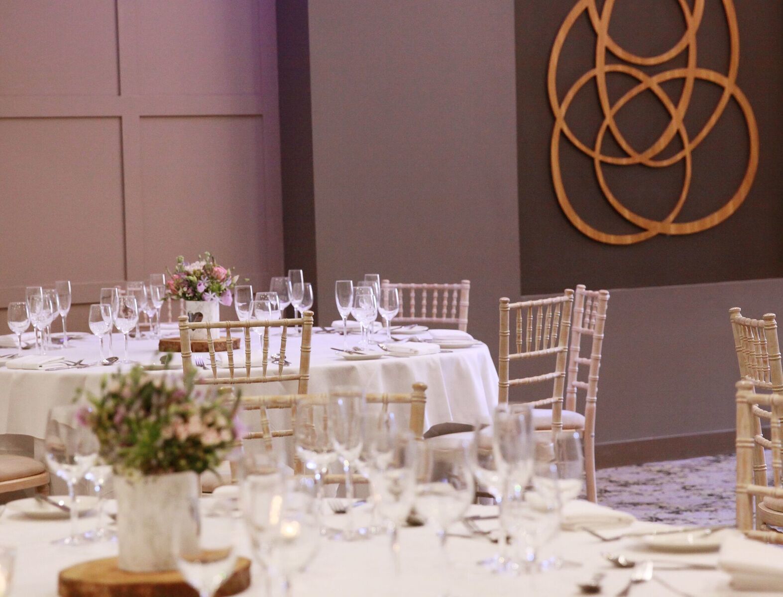 Un salón de banquetes con mesas redondas dispuestas para comer, cada una con manteles blancos y cristalería.