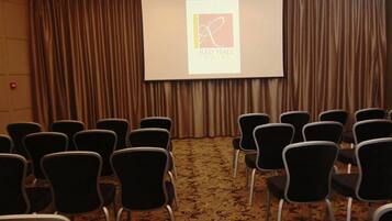 Una sala conferenze con file di sedie rivolte verso uno schermo di proiezione che mostra il logo dell'Hotel Red Hall.