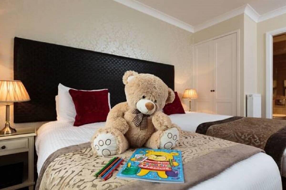 Quarto de hotel com uma cama grande, um urso de pelúcia e um livro infantil sobre a cama.