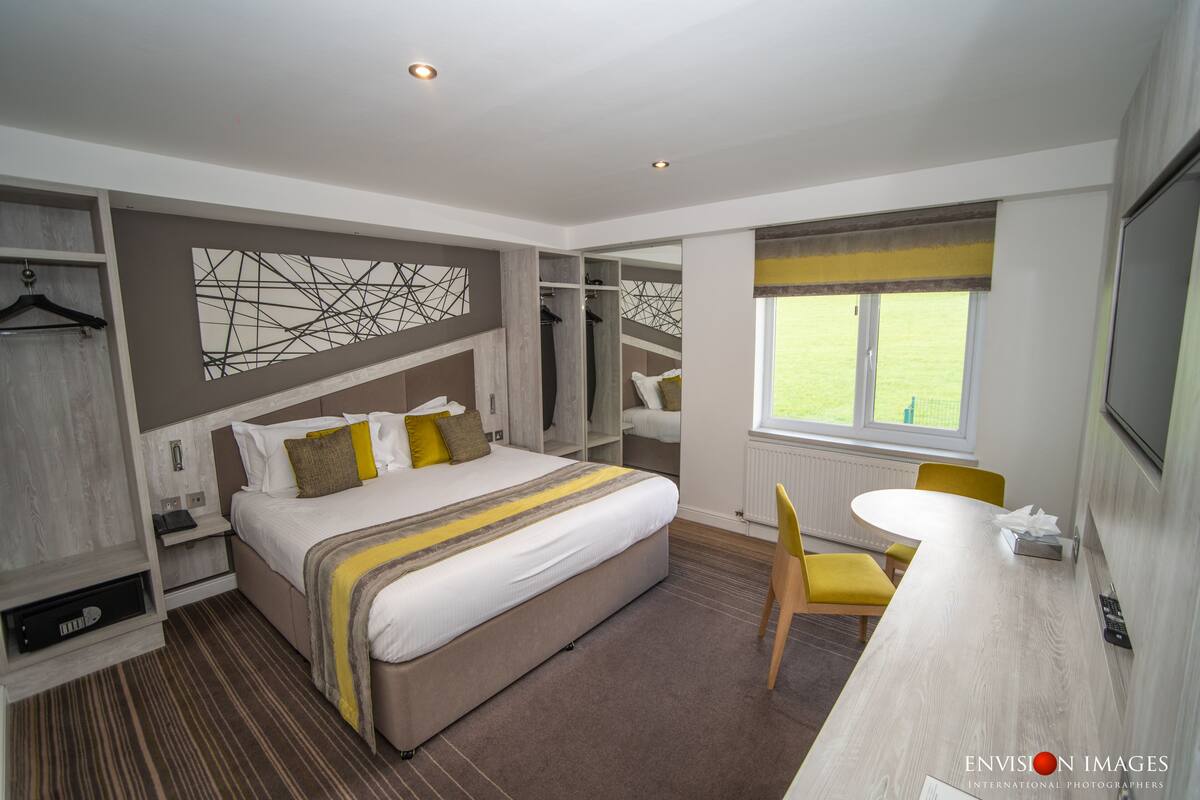 Quarto de hotel moderno com uma cama grande, uma escrivaninha, uma cadeira e vista para o exterior.