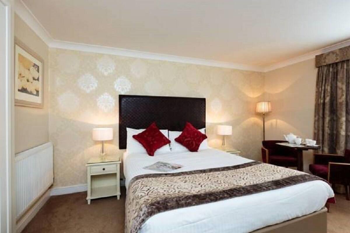 A hotel room with a large bed, two bedside tables with lamps, a small desk, and a chair.