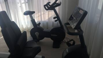 Two stationary bikes with digital displays, a chair, and a window with curtains.
