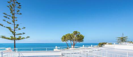 Une terrasse sur le toit offrant une vue dégagée sur la mer, avec des rampes blanches et quelques arbres.