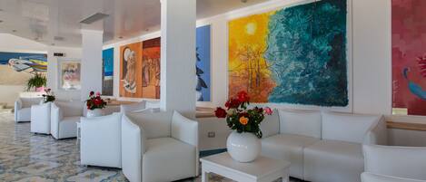 A lobby with white sofas, a tiled floor, and colorful artwork on the walls.