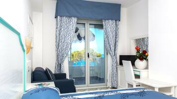Quarto com cama, escrivaninha e cadeira. Tem uma janela com cortinas e vista para o exterior.
