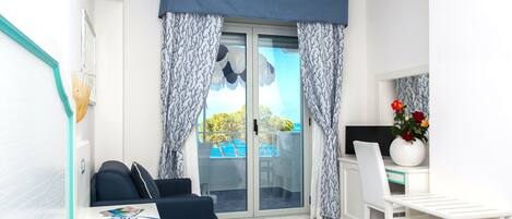 Un dormitorio con cama, escritorio y silla. Hay una ventana con cortinas y vista al exterior.