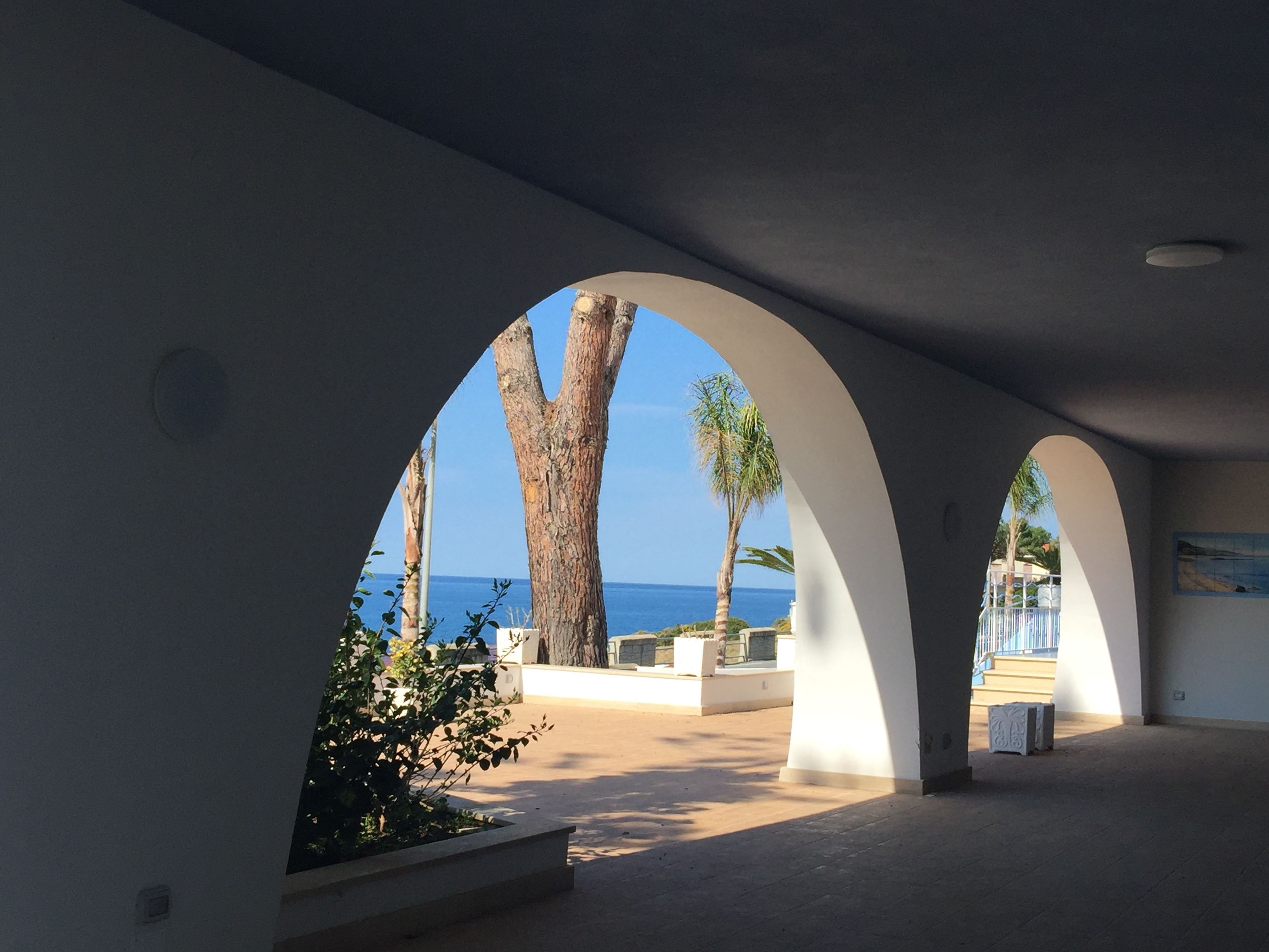 Un couloir intérieur, orné d’arches, qui offre une vue sur la mer.
