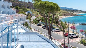 Un hôtel situé sur la côte, doté d’une piscine, offrant une vue sur la plage et donnant sur une route bordée de voitures garées.