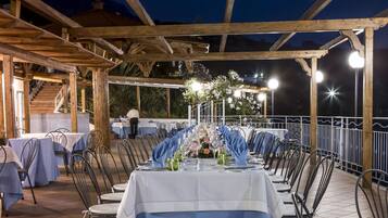 Ein Essbereich im Freien mit gedeckten Tischen, umgeben von Metallstühlen und einer Holz-Pergola.